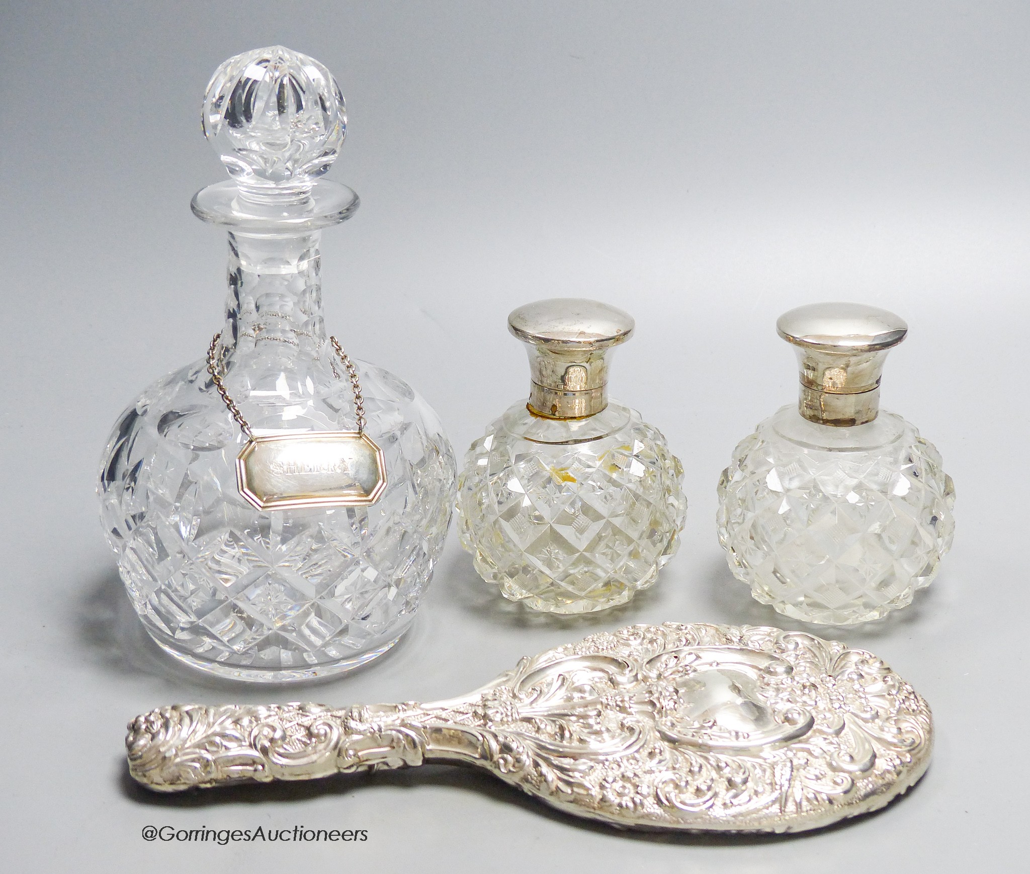 A pair of George V silver mounted scent bottles, (a.f.) 11.6cm, a repousse silver mounted hand mirror and a glass decanter with a silver wine label.